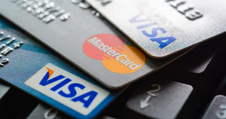 A close range image of three credit cards fanned out on top of a keyboard. The image displays two Visa cards and a Mastercard.